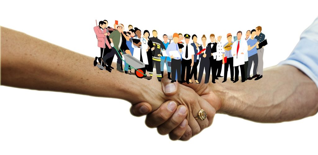 “handshake-3378251_1920.jpg” by geralt is licensed under CC0 Image showing clip art people standing on top of two arms that are connected in a handshake