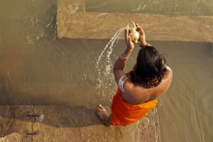 “hindu-1588337_960_720.jpg” by gauravaroraji0 is licensed under CC Image showing a persona pouring water into a larger body of water, as in Worship with Water